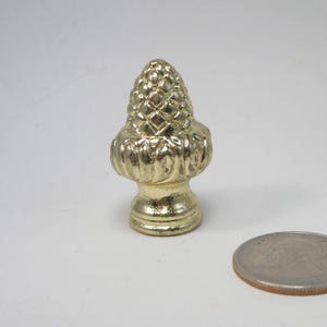 May include: A gold metal finial with a cone-shaped top and a decorative base. The finial is about the size of a US quarter.