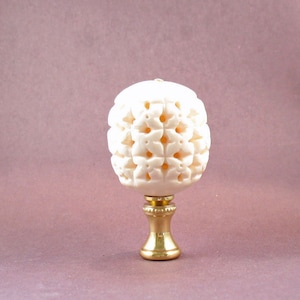 May include: A white ceramic lamp finial with a decorative carved pattern. The finial is mounted on a gold metal base.