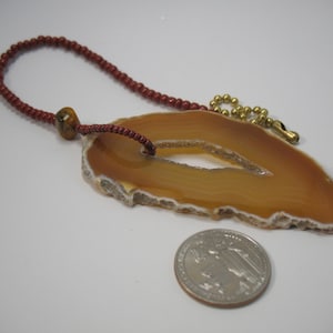 May include: A brown agate slice pendant with a red beaded cord and a gold chain. The pendant is about the size of a US quarter.