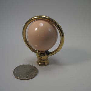 May include: A gold finial with a pink glass orb. The finial is about the size of a quarter.