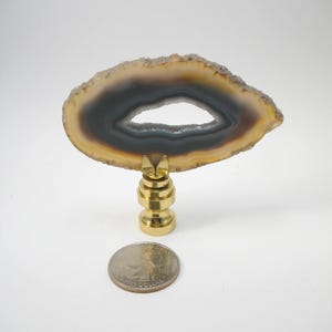 Peut inclure: Un finial de lampe en agate naturelle avec une base en laiton. L'agate est de couleur brun clair avec un centre brun foncé et un trou au centre. Le finial est à peu près de la taille d'une pièce de 25 centimes d'euro.