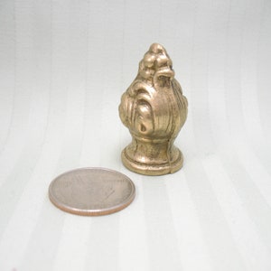 May include: A gold-toned metal finial with an ornate design. The finial is about the size of a UK 20 pence coin.