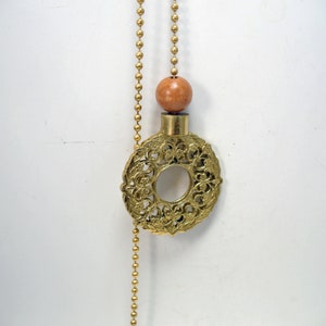 May include: A gold metal decorative chain with a round, ornate, openwork pendant and a wooden bead.