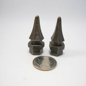 May include: Two antique gold-toned metal finials with a pyramid shape and a detailed base. The finials are about the size of a US quarter.