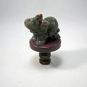 May include: A green and red stone elephant figurine on a purple base with a brass finial. The elephant is standing on all four legs and has its trunk raised.