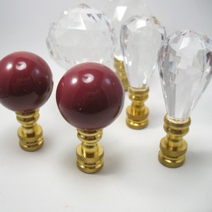 May include: Five lamp finials, two are red and three are clear glass. The finials are all round and have a gold base.