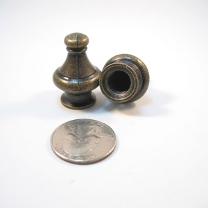 May include: Two antique gold-toned finials, each with a slightly different design, are shown next to a US quarter for size comparison. The finials are approximately 1 inch tall.