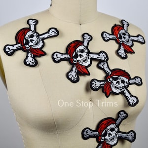 May include: Five white and red embroidered iron-on patches of pirate skulls and crossbones with red bandanas.  The patches are on a white fabric background.