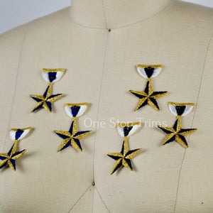May include: Embroidered star-shaped patches with gold, navy blue, and white details. The patches are displayed on a mannequin. The patches have a star shape with a gold border and navy blue centre.