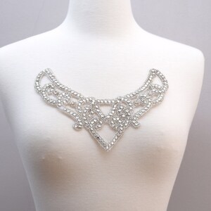 May include: A silver rhinestone embellishment in the shape of a collar. The embellishment is made of small, round rhinestones that are arranged in a delicate, intricate pattern.