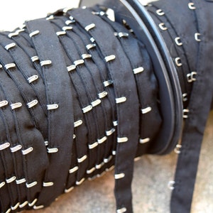 May include: A roll of black fabric with silver metal hooks. The fabric is rolled up on a spool.