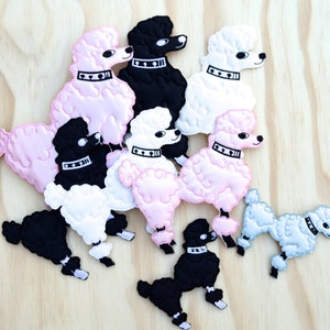 May include: A collection of nine felt poodle patches in pink, white, and black. The patches are all in the same style, with a fluffy, cartoon-like design. They are perfect for adding a touch of whimsy to any project.