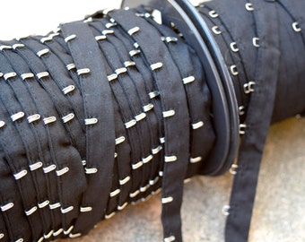 May include: A roll of black fabric with silver metal hooks. The fabric is rolled up on a spool.