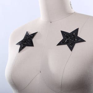 Op de afbeelding: Een witte stoffen mannequin met twee zwarte stervormige versieringen op de borst.