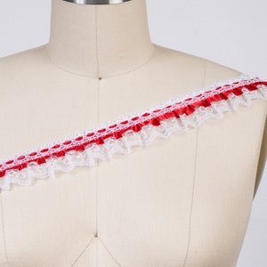 May include: White lace trim with a red satin ribbon and polka dots. The trim is ruffled and has a delicate, feminine look.