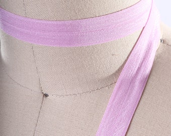 Puede incluir: Primer plano de una banda elástica de color rosa claro. La banda está doblada por la mitad y está sobre una superficie de color marrón claro.