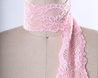 May include: Pink lace trim with a delicate floral pattern. The lace is shown draped over a dress form.