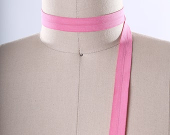 Puede incluir: Una cinta elástica rosa está envuelta alrededor del cuello de un maniquí y cuelga en la parte delantera del maniquí.