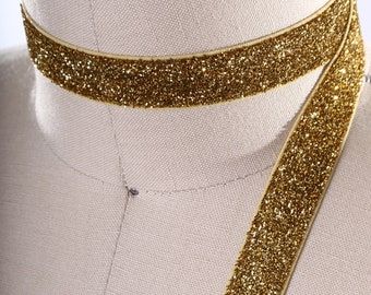 May include: Gold glitter ribbon with a satin finish. The ribbon is shown wrapped around a mannequin's neck and draped down the front.