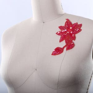 May include: A red sequined flower applique with a leaf design. The applique is made of sequins and beads and is perfect for adding a touch of sparkle to any project.