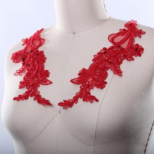 May include: Red lace applique with beaded embellishments. The lace is delicate and intricate, with a floral design. The applique is perfect for adding a touch of elegance to any garment.