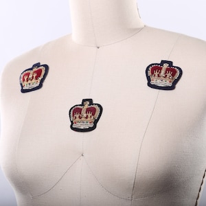 May include: A white fabric mannequin with three gold and red embroidered crown patches. The crowns are in a navy blue fabric.