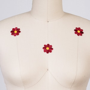 May include: Three red felt flower appliques with yellow centers on a white fabric background.