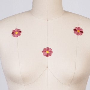Op de afbeelding: Drie roze viltbloem patches met gele centra, genaaid op een wit stoffen mannequin.