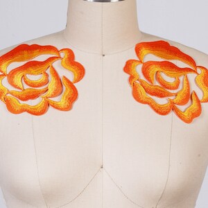 May include: Two orange and yellow embroidered rose appliques. The roses are layered and have a 3D effect.