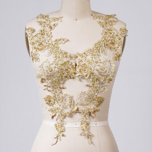 May include: Gold lace applique with a floral design. The lace is delicate and intricate, with a shimmering finish.