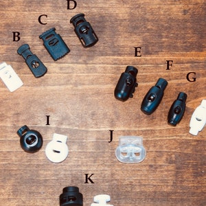 May include: Assortment of 11 plastic slider buckles in black, white, and clear. The buckles are labeled with letters A through K.