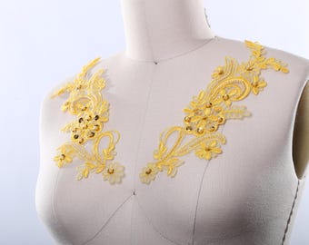 May include: Two gold lace appliques with floral designs and rhinestones. The appliques are on a white fabric background.