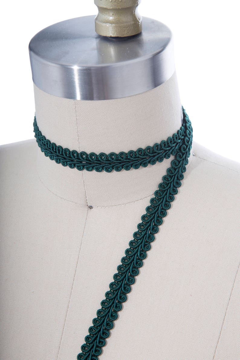 May include: A dark green decorative trim with a scalloped design. The trim is shown wrapped around a dress form.