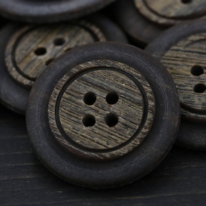 May include: A close-up of a pile of brown wooden buttons with four holes each. The buttons have a dark brown rim and a lighter brown center.
