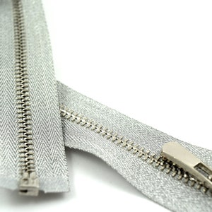 May include: A silver zipper with a silver slider. The zipper is closed and the slider is at the top of the zipper.