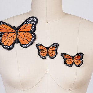 May include: Three embroidered butterfly patches in various sizes. The largest patch is orange with black outlines and white spots. The two smaller patches are orange with black outlines.