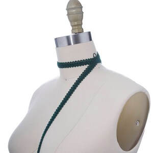 May include: A dark green trim with a decorative pattern is draped over a white dress form.