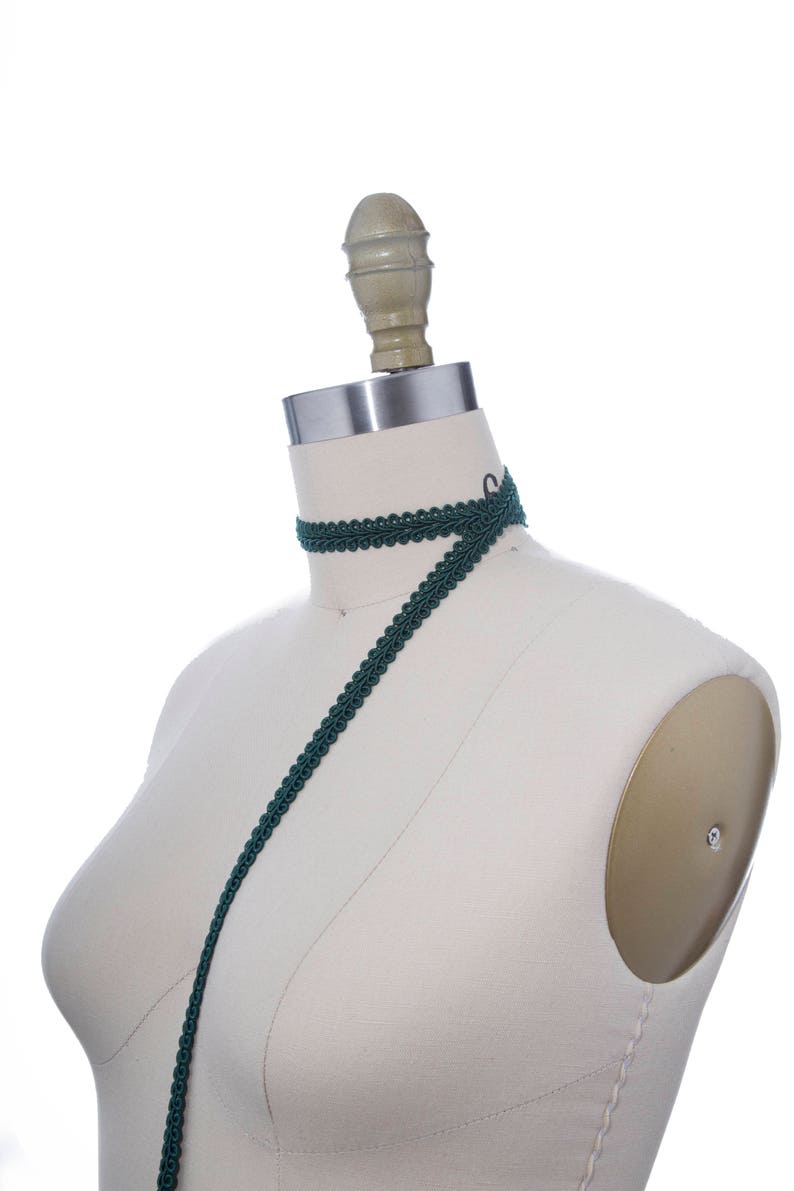 May include: A dark green trim with a decorative pattern is draped over a white dress form.