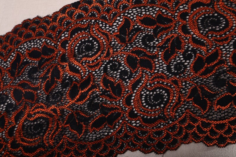 May include: Black lace trim with orange floral embroidery. The lace has a delicate, intricate design.