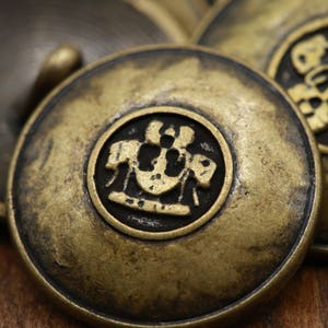 May include: Three antique gold-toned buttons with a raised design. The center button features a crest with a ship's wheel and three figures.