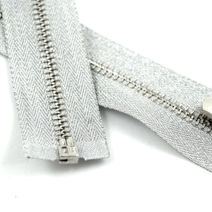 May include: A silver zipper with a metal slider. The zipper tape is a silver color with a herringbone pattern.
