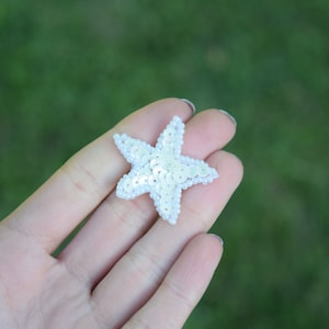 May include: A white sparkly starfish-shaped embellishment. The starfish is made of sequins and is about 2 inches wide.