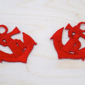 May include: Two red embroidered anchor patches. The anchors are detailed with a rope design and are perfect for adding a nautical touch to any project.