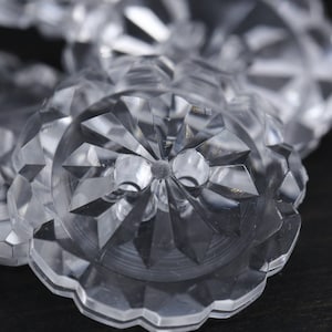 May include: Close-up of a clear, faceted glass button with a starburst design. The button is made of crystal and has a high shine.