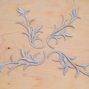 Può includere: Quattro applicazioni decorative a forma di fiore di colore argento su uno sfondo di legno chiaro.