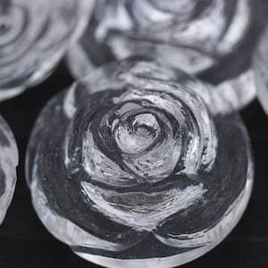 May include: Close-up of clear glass rose-shaped ornaments. The roses are carved with intricate details and have a frosted appearance.