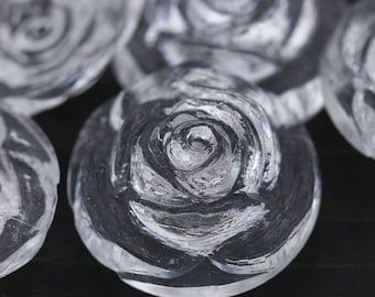 May include: Close-up of clear glass rose-shaped ornaments. The roses are carved with intricate details and have a frosted appearance.