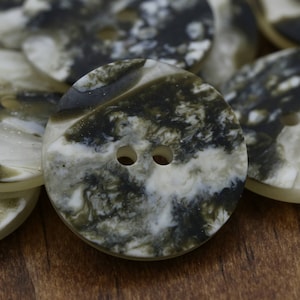 May include: A close-up of two-hole buttons with a white and black marbled pattern. The buttons have a smooth, glossy finish.