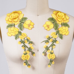 May include: Two yellow floral appliques with green leaves and stems. The appliques are made of embroidered fabric and are perfect for adding a touch of elegance to clothing or crafts.
