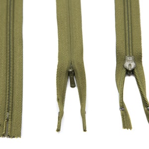 May include: Three green zippers with metal teeth and a slider. The zippers are open and the slider is in the middle of the zipper.
